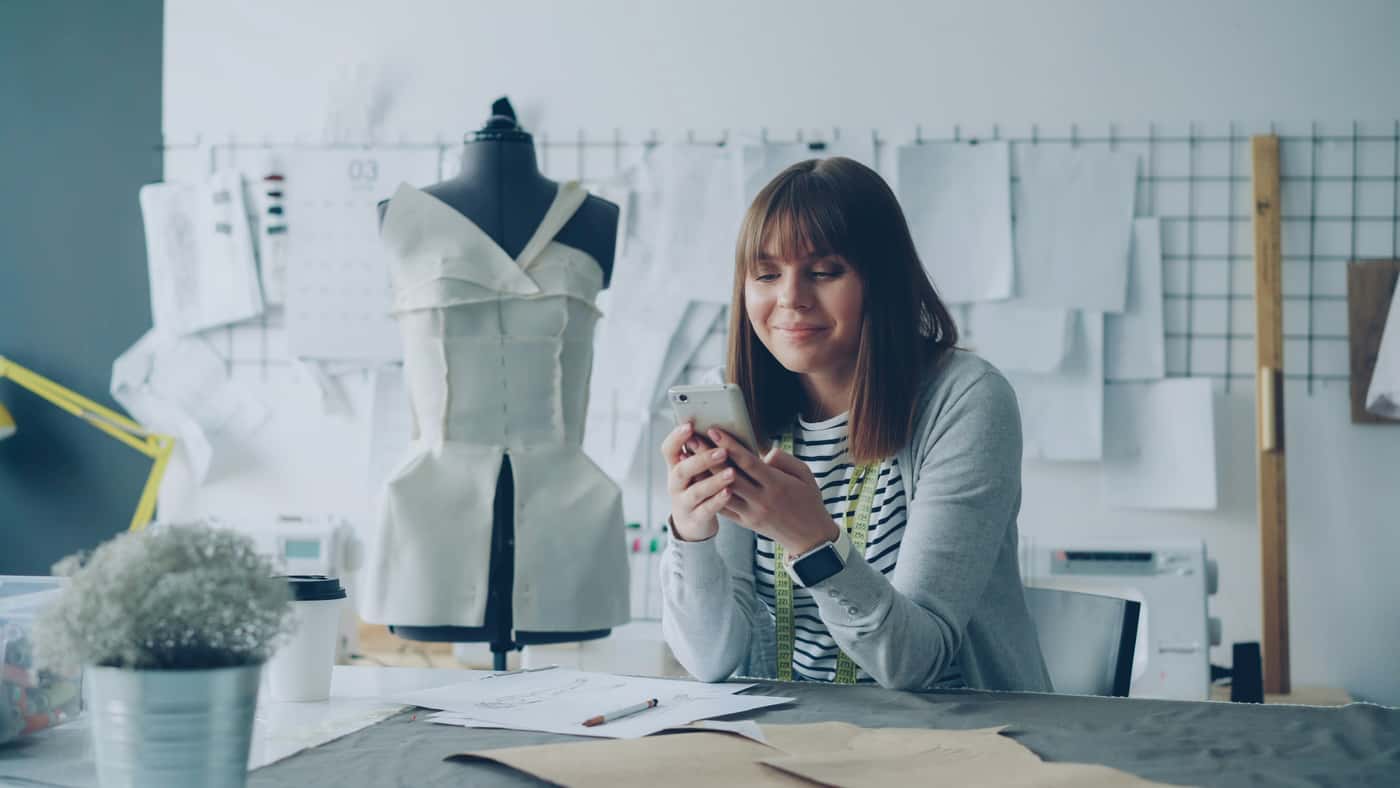 Diseñadora de modas revisando su teléfono en un taller de costura